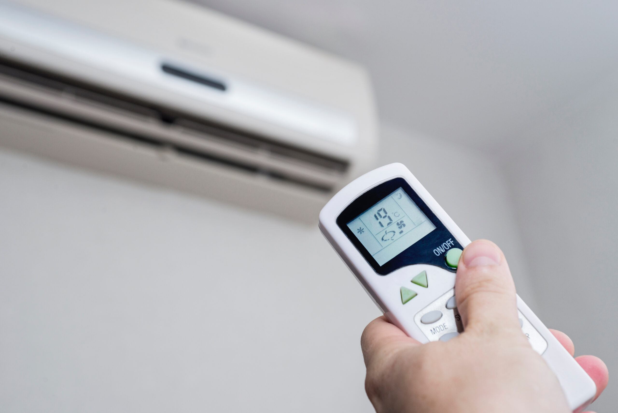 Hand with remote control directed on the conditioner on the wall. Air conditioner with remote controller.